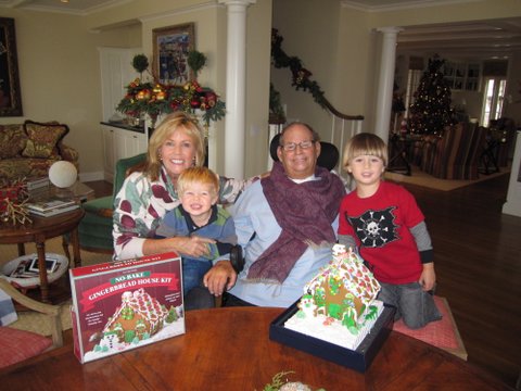 Don and Kathi Koll and two grandkids posing with their homemade gingerbread house.