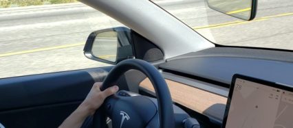 Driving a Tesla with hands on steering wheel.