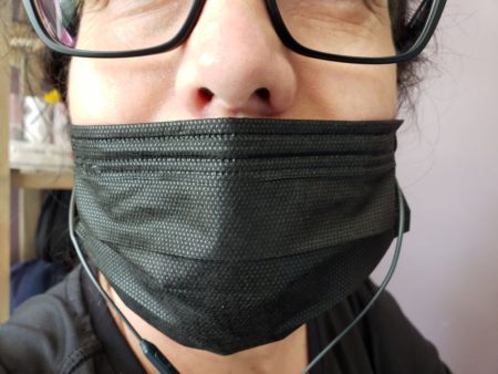Person w black-rimmed glasses and earbuds wearing a black mask