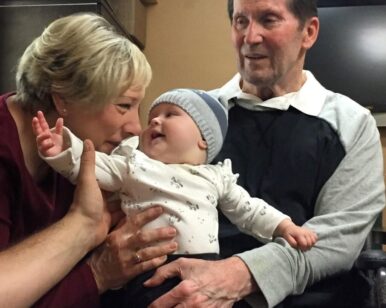 Author, Julie Bennett shares smiles with grandbaby sitting on her husband's lap