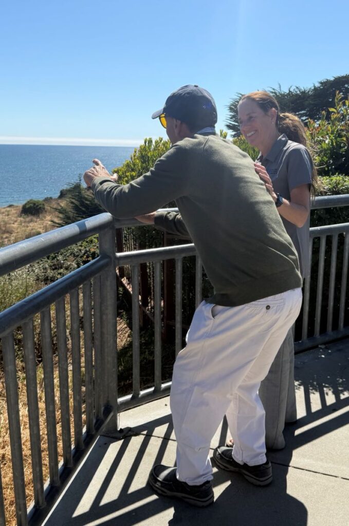 Melissa Mirabello smiling at an older man looking out to the sea below - TCV